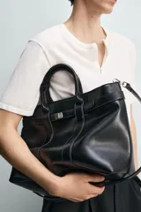 Bolso de mano estructurado en color negro, con diseño minimalista y detalle de cinturón decorativo en la parte superior. Cuenta con doble asa de mano y cierre magnético.