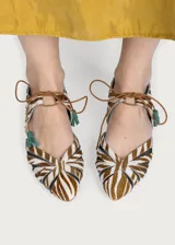 Ballerinas planas Defloresyfloreros modelo Gladiolo, confeccionadas con exterior de cuero con estampado animal print tipo cebra en tonos marrón y blanco, combinado con paneles de rejilla. Cuentan con cordones frontales finos con borlas decorativas verdes y suela de cuero con tacón de 1,5 cm.