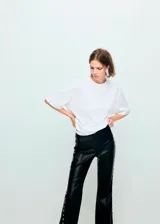 Pantalón de tiro medio efecto piel color negro, de corte flare, con adorno de tachuelas plateadas a lo largo de las costuras laterales.