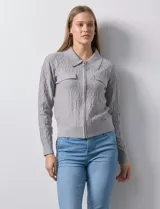 Cardigan de tejido jacquard color gris con diseño geométrico en relieve. Presenta cuello con solapa, cierre frontal completo y bolsillos decorativos en el pecho.