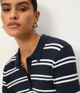 Blusa de punto azul marino con rayas horizontales blancas, cuello polo y cierre frontal con tres botones. Cuenta con mangas cortas.