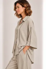 Camisa de lino color beige con cuello camisero, cierre frontal de botones, mangas tres cuartos y detalles de bandas verticales con encaje o calados en el frente y las mangas.