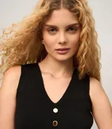 Chaleco sin mangas de tejido de punto negro, con escote en V y cierre frontal mediante una hilera de botones metálicos dorados.