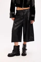 Bermuda sastrera de cuero sintético en color negro, con corte holgado y largo por debajo de la rodilla. Presenta cierre frontal con botón y bolsillos laterales.