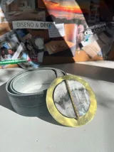 Cinturón gris con textura símil cuero de cocodrilo y hebilla circular dorada con piedra ágata en tonos grises y blancos.