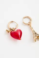 Par de aros tipo argolla dorados con diseño asimétrico. Uno de los aros presenta un dije de corazón rojo de vidrio y el otro un dije metálico con forma de la Torre Eiffel.