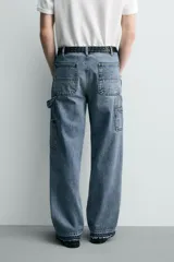 Pantalón de jean estilo carpintero con corte relaxed fit, tiro medio y pierna recta. Presenta un lavado azul medio con efecto desgastado y roturas en las rodillas. Incluye bolsillos laterales tipo plastrón, tira multifunción en la pierna, cierre frontal con cremallera y botón.