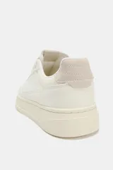 Zapatillas deportivas de mujer, color blanco hueso, con detalles en tono beige claro en el talón y paneles laterales. Presentan una suela de plataforma gruesa y cierre con cordones.