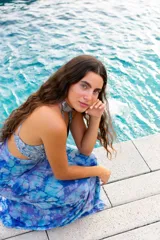 Vestido largo con estampado tie-dye en tonos violeta y fucsia, escote en V con detalles bordados dorados, cut-outs laterales bajo el busto y tirantes finos que se cruzan y atan en la espalda.