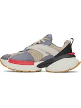 Championes Under Armour modelo UA Arc 96, con diseño futurista de inspiración retro. Capellada de malla múltiple en tono beige con superposiciones de cuero y paneles laterales translúcidos. Incorpora detalles en gris, negro y un toque de rojo, con entresuela voluminosa y suela de goma color caramelo.