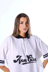 Chomba blanca de pique con cuello y solapa negros, cierre frontal parcial y mangas cortas con ribetes negros. Estampado frontal en cursiva negra.