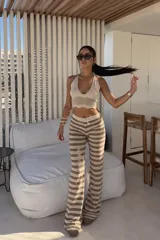 Conjunto de dos piezas de tejido de punto calado, compuesto por un top halter corto en color marfil y un pantalón largo de tiro medio con patrón de rayas horizontales en tonos marrones y beige.