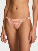 Panty tipo bikini confeccionado en encaje supersuave color salmón, con diseño de talle bajo, herrajes de mariposa de cristal en los laterales y espalda de malla transparente con fruncido.