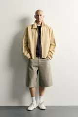 Cazadora regular fit de color beige, confeccionada en mezcla de algodón y lyocell. Cuenta con cuello camisero, cierre frontal de cremallera, bolsillos de plastrón en la cadera, mangas largas con puños elásticos y bajo con ajuste elástico.