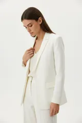 Blazer de lino color blanco, con cuello solapa, bolsillos delanteros con solapa y corte holgado.