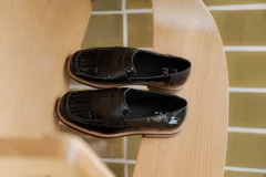 Mocasines negros de cuero con textura tipo cocodrilo en la parte superior y acabado brillante. Presentan una banda frontal clásica y una suela plana con detalle de borde en color natural.