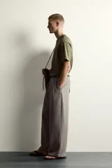 Pantalón relaxed fit de color blanco off-white, confeccionado en tejido con lino. Cuenta con pliegues frontales en la cintura, bolsillos delanteros y cierre frontal con cremallera y botón.