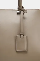 Bolso tipo city de diseño estructurado, con doble asa de mano y asa bandolera extraíble. Cuenta con doble compartimento exterior con cierre de cremallera metálica y un compartimento central con cierre imantado. Incluye un detalle de etiqueta colgante en el asa.