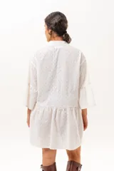 Vestido corto de broderie color crudo, con cuello camisero, cierre frontal parcial con botones, mangas tres cuartos acampanadas y corte evasé con volados.