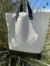 Bolso tote de lona color crudo con base y asas de cuero negro.