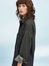 Camisa de denim azul de corte oversize, con mangas largas, cuello clásico, un bolsillo aplicado en el pecho y cierre frontal con botones metálicos.