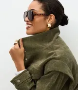 Campera de pana cotelé color verde militar, con cuello camisero, cierre frontal con botones metálicos y bolsillos frontales con solapa. Presenta diseño de sisa desplazada y cordones ajustables en el ruedo.