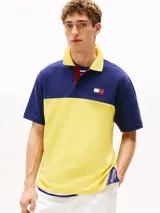 Chomba Tommy Hilfiger de corte amplio, con diseño color block en azul y amarillo, cuello clásico, cartera de tres botones, logo bordado en el pecho y logo oversize en la espalda.