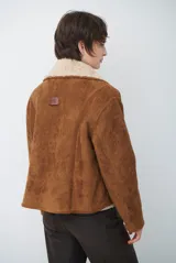 Chaqueta tipo gamulán de color marrón, con solapas amplias forradas en corderito sintético oscuro. Presenta un diseño cruzado con botones frontales y mangas largas, ideal para un estilo invernal.