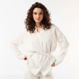 Camisa larga blanca de lino, con cierre frontal de botones, mangas largas y lazo ajustable en la cintura.