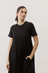 Vestido midi negro con diseño de manga corta, cuello redondo y bolsillos laterales, corte amplio y fluido.