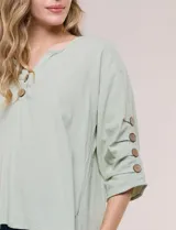 Blusa Erika de algodón con estampado de rayas en tonos azules, rosados y amarillos. Presenta cuello redondo con escote en V y botones frontales, mangas cortas decoradas con una fila de botones en los laterales y dobladillo asimétrico.