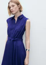 Vestido midi de corte evasé y diseño sin mangas, confeccionado en tejido texturizado color azul. Presenta cuello camisero, cierre frontal con botones, bolsillo de parche en el pecho y un lazo ajustable en la cintura.