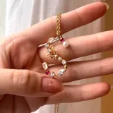 Cadena dorada con dije de letra S grande, con piedras blancas, rosas y rojas, y perla engarzadas.