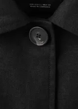 Chaqueta de lino color negro con diseño recto, cuello camisero, manga larga, cierre frontal de botones y cinturón ajustable del mismo material. Incluye forro interior.