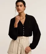 Camisa negra de viscosa sostenible, con escote en V, mangas largas abullonadas con puños elásticos y cierre frontal con botones. Presenta detalles de canalé en los hombros y la espalda.