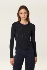 Sweater de punto fino en color negro, con diseño de canalé, cuello redondo y mangas largas. Presenta un corte ajustado con aberturas laterales en el ruedo y está decorado con pequeñas cuentas doradas en la parte frontal.