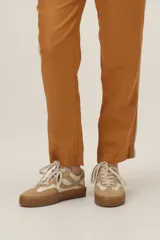 Championes urbanos de cuero en combinación de tonos beige y tostado, con detalle de tachas metálicas en los laterales y suela de goma texturizada en color caramelo.