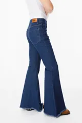 Pantalón de jean azul oscuro, corte acampanado (flare) de tiro alto, con costuras visibles en contraste y bordados tonales en la parte inferior de las piernas. El ruedo es deshilachado.