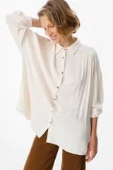 Camisa de corte oversize color chocolate, con cuello clásico, cierre frontal de botones y mangas largas con puños abotonados. Presenta un diseño fluido y holgado con sutiles frunces en los hombros.