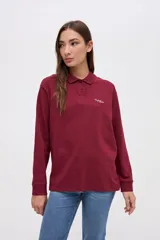 Remera tipo polo de manga larga en color beige, confeccionada en algodón pesado con textura suave. Presenta cuello clásico, cierre frontal con botones y un pequeño bordado en el pecho. Posee puños en las mangas y un corte relajado.