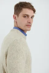 Sweater de tejido de punto color beige claro, con diseño de trenzas (aranes) en el frente y mangas de punto liso. Tiene cuello redondo.