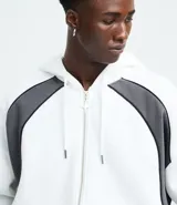 Saco con capucha y cierre frontal de cremallera, confeccionado en tejido de algodón y poliéster. Presenta un diseño bicolor con cuerpo blanco y paneles laterales en gris oscuro, mangas largas y bolsillos delanteros.