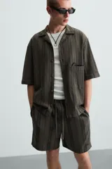 Bermuda de algodón color blanco, de corte relajado (relaxed fit), con cintura elástica ajustable mediante cordón. Posee bolsillos laterales y un bolsillo trasero de plastrón. Presenta un bordado en contraste en la pernera.