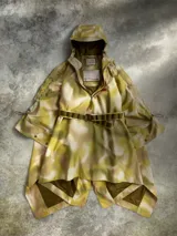 Poncho impermeable de diseño técnico con estampado camuflado en tonos tierra, cuello alto con cierre frontal parcial, capucha integrada y cinturón ajustable con compartimentos. Incluye parches decorativos en el pecho.