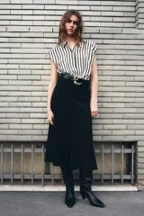 Vestido midi de diseño combinado con cuerpo de camisa sin mangas a rayas verticales en blanco y negro, y falda negra de corte recto. Presenta cuello solapa, cierre frontal con botones y cinturón negro con hebilla metálica dorada.