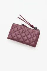 Billetera o monedero acolchado color vino tinto, con costuras en patrón de rombos. Presenta un cierre de cremallera y una correa de mano trenzada en tonos vino y blanco. El nombre de la marca está grabado en relieve en la parte frontal.