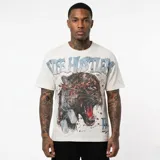 Remera de corte oversize color blanco con estampa frontal de un leopardo con una flecha, placas de identificación militar y texto superior con efecto brillante.