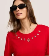 Remera de viscosa color rojo, corte clásico, con cuello redondo y mangas cortas. Presenta aplicación de strass en el escote.