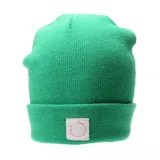 Gorro tipo beanie tejido en color verde, con vuelta y etiqueta frontal blanca con texto circular en color rosa.