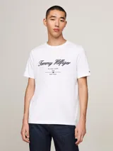 Remera de algodón Tommy Hilfiger, color blanco, con cuello redondo y manga corta. Presenta el logo de la marca bordado en el pecho en tipografía cursiva y la bandera distintiva bordada en la manga.